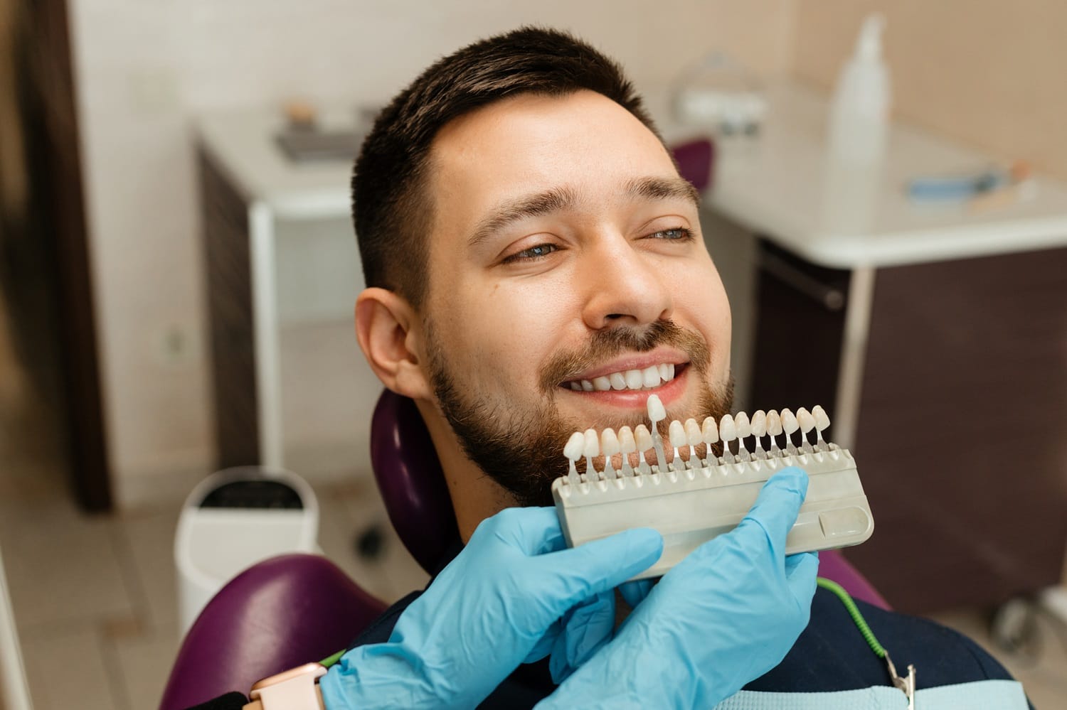 Teeth Shade Matching – Dentist in San Mateo Smiling man at the dentist having his tooth color matched with a shade guide for veneers or whitening — Dentist in San Mateo